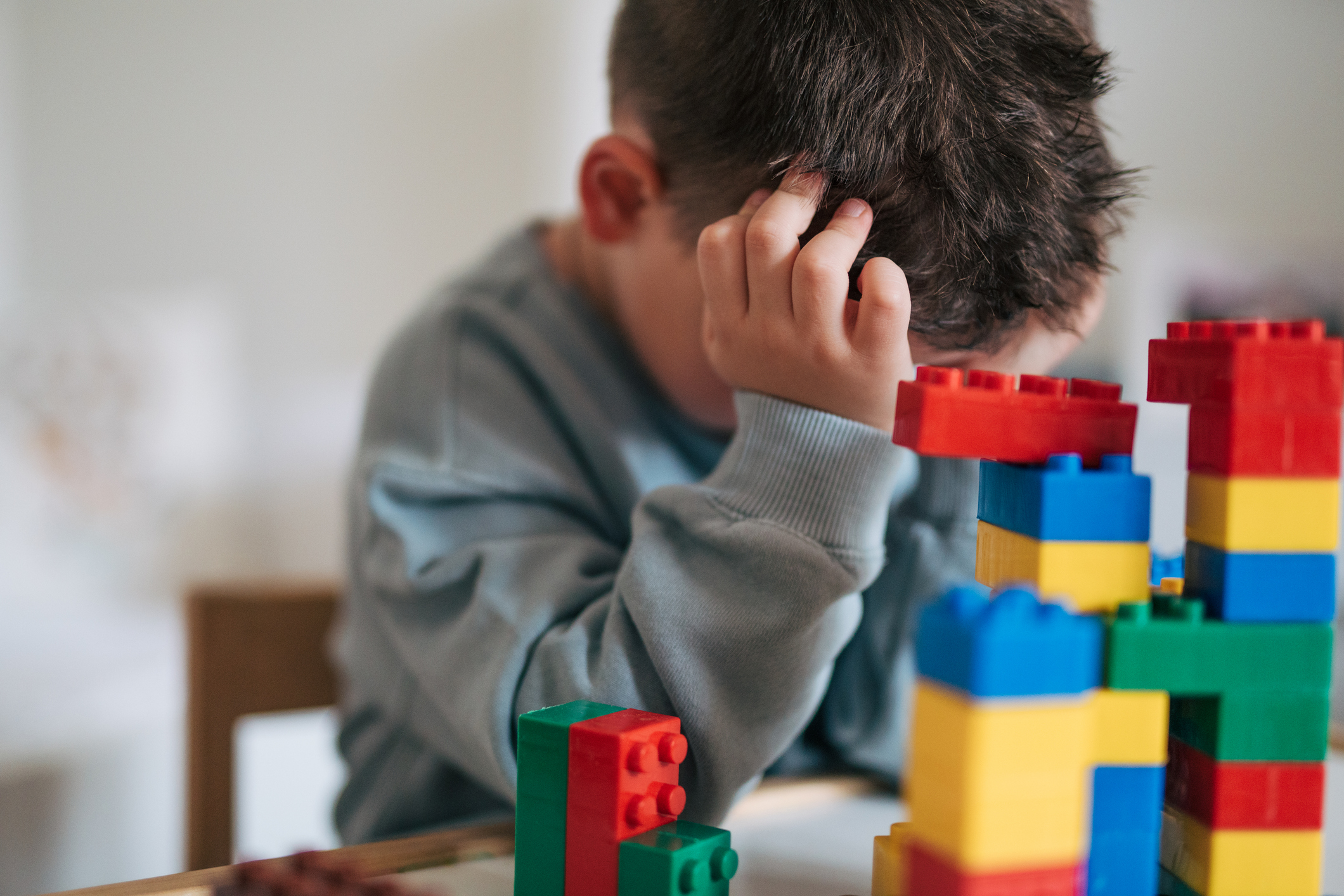 Little boy covering his face with his hands. Building blocks can be seen in the foreground.